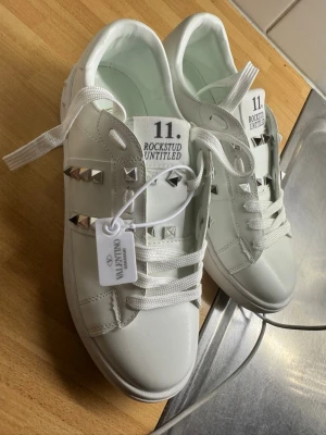 Valentino Rockstud vita sneakers - Snygga vita sneakers från Valentino med silverfärgade nitar och coola detaljer. Modellen heter Rockstud Untitled och har en chunky sula samt vita skosnören. Tillverkade i läder för en lyxig känsla och unik look.