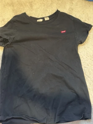 Svart t-shirt från Levi's - Klassisk svart t-shirt från Levi's med rund halsringning och liten röd Levi's-logga på bröstet. T-shirten har korta ärmar och är gjord i mjuk bomull, perfekt för en enkel och stilren look.