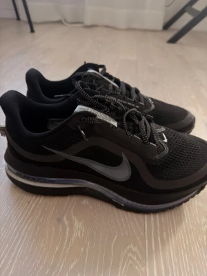 Nike Pegasus svarta sneakers - Snygga svarta Nike Pegasus sneakers med mesh-ovandel och reflekterande detaljer. Skorna har en tydlig swoosh-logga på sidan, svart sula med synlig dämpning och klassiska snören med mönster. Perfekta för dig som gillar sportig och stilren look.