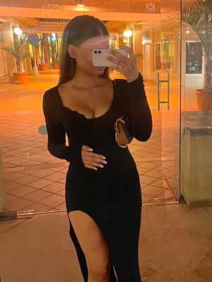 Svart långklänning med slits - Snygg svart långklänning med djup v-ringning och lång ärm. Klänningen har en hög slits på ena sidan som går att framhäva men även justera bort och dra åt sidan. Bekvämt material med stretch. 