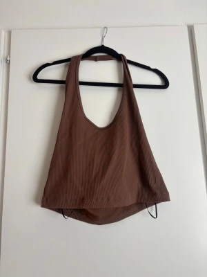 Brun ribbad halter neck topp - Säljer en brun ribbad halter necktopp med djup urringning och breda axelband. Toppen är croppad och har en avslappnad passform, perfekt för varma dagar eller lager på lager. Materialet är mjukt och stretchigt för extra komfort.