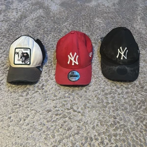 Tre kepsar: NY & Goorin Bros - Säljer tre kepsar: en röd New Era 9FORTY med New York Yankees-logga, en svart New Era med Yankees-logga och en vit/svart Goorin Bros truckerkeps med Cash-motiv. Alla har böjd skärm och justerbar passform. Perfekt för dig som gillar streetwear och sportig stil.                          Den röda:100kr, Den svarta:50kr, Den vita:50kr.     Alla:125kr