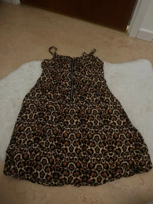 Leopardmönstrad klänning H&M Divided - Leopardmönstrad kort klänning från H&M Divided med smala axelband och dragkedja framtill. Klänningen har en figurnära passform och är tillverkad i ett mjukt bomullsmaterial. Perfekt för dig som vill sticka ut med ett djurmönster.