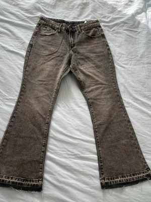 Bruna bootcut jeans från New Yorker - Säljer ett par bruna bootcut jeans från New Yorker med slitna detaljer och rå kant längst ner. Jeansen har klassisk femficksmodell och är tillverkade i denim med en lätt tvättad look. Perfekta för en avslappnad och trendig stil.