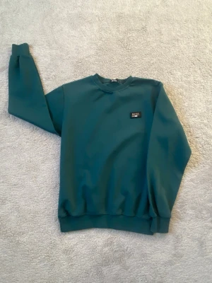 Mörkgrön sweatshirt från BOSS - Mörkgrön sweatshirt från BOSS med rund halsringning och ribbade muddar vid ärmslut och nederkant. Klassisk logopatch på bröstet. Perfekt för en avslappnad och stilren look.