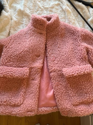 Rosa Teddy jacka  - Jättemysig teddyjacka i fin rosa färg 🧸💕 Storlek S, men modellen är något oversized vilket ger en trendig och avslappnad look. Perfekt både som jacka under mildare dagar eller som ett extra lager när det är kallt.  Materialet är supermjukt och fluffigt, vilket gör den väldigt bekväm att bära hela dagen. Den har en stilren design med stora fickor som både är praktiska och snygga ✨  Jackan är i mycket bra skick utan synligt slitage.  En perfekt jacka för dig som vill ha något både bekvämt och tren