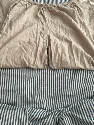 Beiga vida linnebyxor med resår - Säljer ett par beiga linnebyxor med avslappnad passform och resår i midjan. Byxorna har raka ben och sidofickor, perfekta för en chill och luftig stil. Materialet är tunt och svalt linne, vilket gör dem riktigt sköna under varma dagar. Kommer att strykas när jag skickar iväg den 