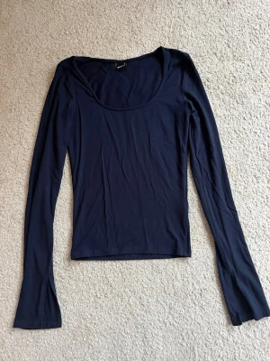 Mörkblå långärmad topp Gina Tricot - En stilren mörkblå långärmad topp från Gina Tricot med rundad, djup ringning. Tunn och mjuk i materialet, perfekt att styla till jeans eller kjol. Enkel design som funkar till många olika looks.