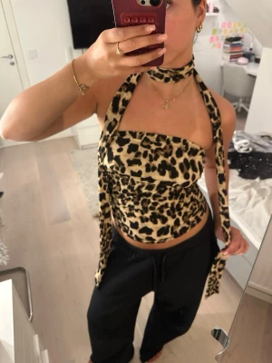 Leopardmönstrad bandeau topp - Snygg bandeau topp med leopardmönster och matchande scarf runt halsen. Toppen är ärmlös och har en croppad passform, perfekt för att sticka ut. Mjuk och stretchig känsla, passar dig som gillar trendiga statement-plagg. Storlek M men passar även S, använd 2 gånger.