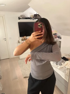 Grå oneshoulder topp från Zara i storlek S - Snygg grå topp med oneshoulder-design och lång ärm från Zara i storlek S. Hela ryggen är genomskinlig, men man ser inte alls igenom på framsidan! Fin detalj på ärmen 