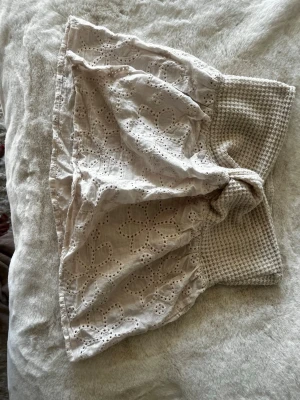 Beige bandeau tubtopp med broderi - Beige bandeau tubtopp med bred smockad resår och broderade blommor i hålmönster. Toppen är ärmlös och har en luftig och feminin känsla, perfekt för sommaren. Tillverkad i bomull.Den är ifrån SHEIN.