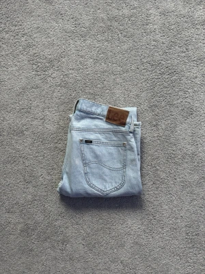 Ljusblå jeans från LEE - Säljer ett par ljusblå jeans från LEE med klassisk femficksdesign och brunt läderpatch bak i midjan. Jeansen har raka ben och är tillverkade i denim av bomull. Perfekta för en avslappnad och trendig stil. Perfekt som söker ett par jeans mellan ”baggy” och ”slim”. Super bra skick dessutom så dom knappt används. Bara att höra av dig vid frågor🌟