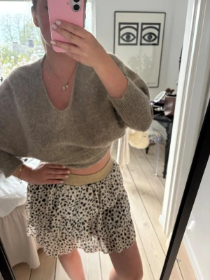 Beige kortkjol med leopardmönster - Snygg kortkjol i beige med svart leopardmönster och glittrig guldresår i midjan. Kjolen har en luftig och lätt känsla, perfekt för dig som vill sticka ut med en trendig look.