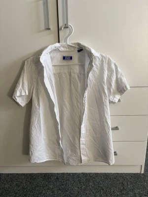 Vit kortärmad skjorta Jack & Jones - Vit skjorta från Jack & Jones med korta ärmar och klassisk krage. Skjortan är tillverkad i bomull och har en enkel, stilren design utan mönster. Perfekt för en avslappnad och fräsch look.