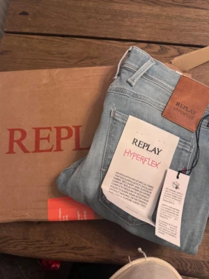 Replay Hyperflex ljusblå jeans - Säljer ett par ljusblå jeans från Replay Hyperflex med klassisk femficksdesign och snyggt läderpatch bak. Jeansen är tillverkade i ett stretchigt material som ger grym rörelsefrihet och komfort. Perfekt för dig som vill ha både stil och flexibilitet.