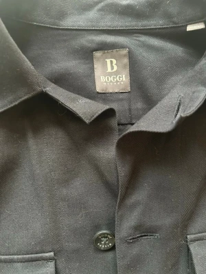 Svart overshirt från Boggi Milano - Säljer min overshirt knappt använd sedan köpt därför jag säljer den. Skicket är 10/10 nypris 2500kr säljer för 1800kr priset är inte hugget i sten