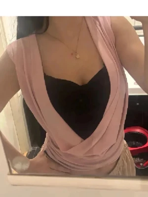 Rosa omlottopp med djup urringning - Snygg rosa omlottopp med djup v-ringning och ärmlös design. Toppen har en draperad framsida och bärs här med ett svart linne under. Perfekt för dig som gillar trendiga och feminina plagg. Svarta under sitter fast😊