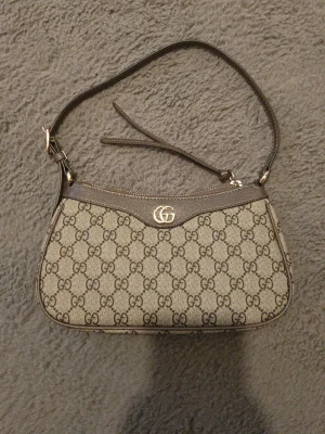 Gucci ophidia 25 small - Snygg axelväska från Gucci i beige canvas med klassiskt GG-monogram över hela väskan. Väskan har bruna läderdetaljer, justerbar axelrem och guldfärgad GG-logga framtill. Perfekt storlek för det viktigaste och stängs med dragkedja.