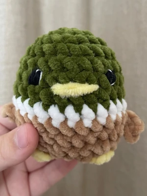 Handvirkad anka i chenille – ca 10 cm - Handvirkad anka i mjukt chenillegarn i gröna, vita och bruna toner med små vingar och gul näbb. En liten och charmig plushie som passar perfekt som present eller som gullig inredningsdetalj. Varje exemplar är unikt och gjort helt för hand. Ca 10 cm hög.