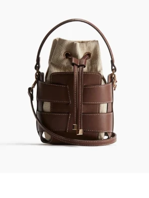 Brun och beige bucket bag i läder - Trendig bucket bag med brunt läderhölje och beige canvasinsats. Väskan har justerbar axelrem, handtag och snygga gulddetaljer. Stängs med dragsko och har en unik, modern design som sticker ut.