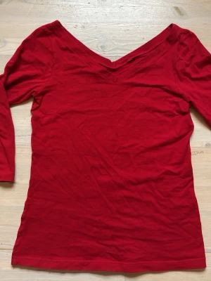 Röd topp med v-ringning - Snygg röd topp med v-ringning både fram och bak och trekvartsärm. Modellen är figurnära och enkel, perfekt att styla med jeans eller kjol. Tillverkad i mjukt bomullstyg som känns skönt mot huden. Köpt second hand och vet varken storlek eller märke, men  ser ut att vara i mycket fint skick! Passar nog både xs - m, töjbar. Älskar den röda färgen :)