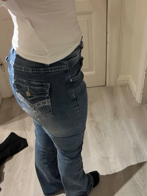 Blå bootcut jeans med detaljer - Säljer ett par blå bootcut jeans med snygga vita sömmar och dekorativa fickor. Säljer för dem är för stora för mig så aldrig använda 