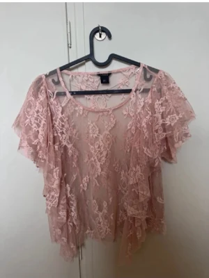Rosa spetsblus från lindex - Söt ljusrosa blus i spets från lindex med korta, volangiga ärmar och transparent material. Perfekt för dig som gillar romantisk stil och vill ha något luftigt och lätt. Blusen har rund halsringning och fina spetsdetaljer över hela plagget.
