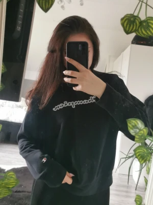 Svart Champion sweatshirt - Säljer en svart sweatshirt från Champion med det klassiska logotyptrycket på bröstet och en liten logga på ärmen. Tröjan har rund halsringning och lång ärm. Perfekt för en avslappnad och sportig stil.