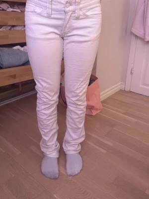 Vita  jeans med låg midja - Säljer ett par vita jeans med låg midja och klassiska femficksdetaljer. Jeansen har smal passform hela vägen ner och är tillverkade i stretchigt denimtyg för en bekväm känsla. De är ifrån J.lindeberg