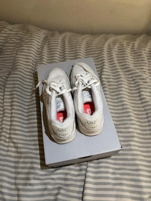 Vita Nike Air Max 90 sneakers - Säljer ett par klassiska vita Nike Air Max 90 sneakers med mesh och läderdetaljer. Skorna har den ikoniska Air-sulan och snygga detaljer som swoosh-logga på sidan och broderad Nike Air-text på hälen. Perfekta för dig som gillar stilrena och tidlösa sneakers. (Pris går att diskutera)