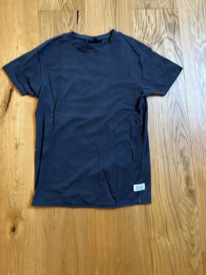 Mörkgrå t-shirt från SMOG - En stilren mörkgrå t-shirt från SMOG Original. Slimmad passform med rund hals och korta ärmar. Tillverkad i mjuk bomull som känns skön mot huden. Perfekt basplagg till alla outfits och enkel att matcha.