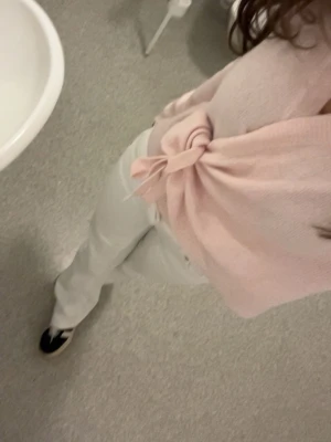 Ljusrosa omlottkofta med knytband - Supersöt ljusrosa omlottkofta med knytband i sidan och långa ärmar. Koftan har en mjuk och stickad känsla, perfekt att slänga på sig över en topp. Enkel och feminin design som passar till många outfits.