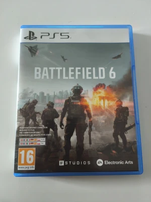Battlefield 6 till PS5 - Battlefield 6 till PlayStation 5 med blå plastfodral. Omslaget visar soldater, explosioner och stridsflygplan mot en stad i bakgrunden. Spelet är ett actionfyllt FPS utvecklat av BF Studios och Electronic Arts. PEGI 16.