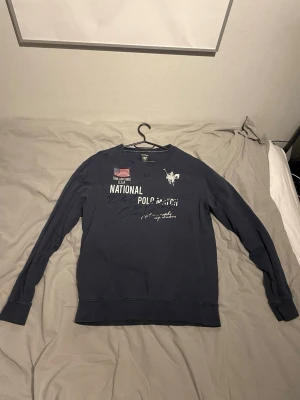 Mörkblå sweatshirt från Vinson Polo Club - Mörkblå sweatshirt med tryck framtill från Vinson Polo Club. Tröjan har rund halsringning, långa ärmar och vita detaljer med logga och text. Tillverkad i mjukt bomullsmaterial, perfekt för en avslappnad och stilren look.