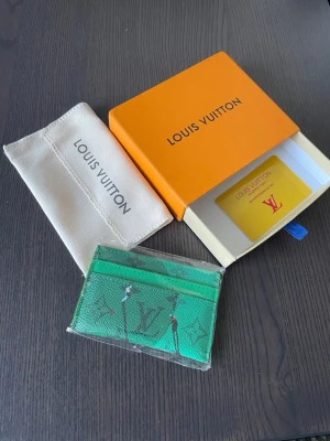 Grönt kortfodral - Snyggt grönt kortfodral från ett välkänt märke med monogrammönster och lekfullt tryck. Tillverkad i tåligt läder och levereras med original ask och dustbag. Perfekt för kort och ID, smidig att ha i fickan eller väskan.