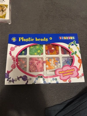 Playbox färgglada plastpärlor - Säljer ett set med färgglada plastpärlor från Playbox. Innehåller pärlor i olika former och färger som rosa, grön, orange, lila och röd. Perfekt för att skapa egna smycken som armband och halsband. Allt kommer i en praktisk förpackning med flera fack.