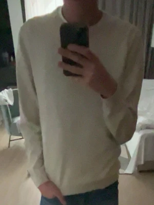 Beige Sweater - En stilren beige tröja med rund hals och långa ärmar. Tröjan är tillverkad i mjuk bomull och har ribbade muddar vid ärmslut och nederkant. Perfekt för en enkel och clean look.
