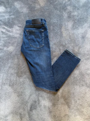 Jack & Jones Jeans - Snygga blå slim fit jeans från Jack & Jones med klassisk femficksdesign och läderpatch bak i midjan. Jeansen har raka ben och är tillverkade i mjuk denim med lätt tvättad look. Perfekta för en avslappnad och trendig stil.