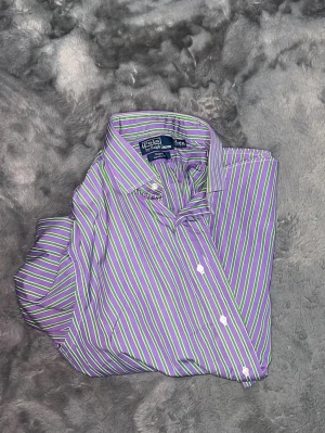 Polo Ralph Lauren Striped Shirt – Purple & Green -  Klassisk och superfresh skjorta från Polo Ralph Lauren i en unik och iögonfallande färgkombination med lila, gröna och vita ränder. Modellen är "Regent Classic Fit" vilket ger en skön och avslappnad siluett. • Märke: Polo Ralph Lauren • Modell: Regent Classic Fit • Färg: Lila, Grön, Vit •  Skick: Toppskick och fräsch!