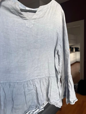 Ljusblå volangblus från Replay - Supersöt ljusblå blus från Replay i ett luftigt linnematerial. Blusen har långa ärmar, v-ringning och volangdetalj nedtill som ger en avslappnad och trendig look. Perfekt att styla med jeans eller kjol.  Passar en M.