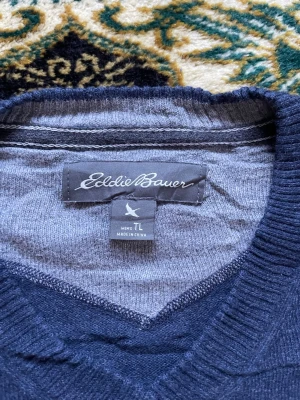 Mörkblå stickad tröja Eddie Bauer - Mörkblå stickad tröja från Eddie Bauer med v-ringning och långa ärmar. Tröjan är enkel och stilren, perfekt för lager-på-lager och passar till många olika outfits. Mjukt material som känns skönt mot huden.