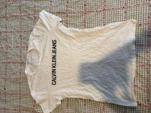 Vit t-shirt från Calvin Klein Jeans - Vit t-shirt från Calvin Klein Jeans med svart tryck på framsidan. 
