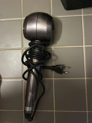 Svart locktång från Curls Secret - Elektrisk locktång i svart och grått från Curls Secret. Har ett runt huvud där håret automatiskt dras in för att skapa lockar. Utrustad med sladd och europeisk kontakt. Perfekt för att snabbt fixa snygga lockar hemma.