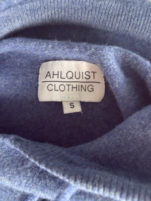 Blå stickad tröja från Ahlquist - Mysig blå stickad tröja från Ahlquist Clothing i storlek S. Tröjan har rund halsringning och dragsko med metalländar. Perfekt för dig som gillar en enkel men stilren look.