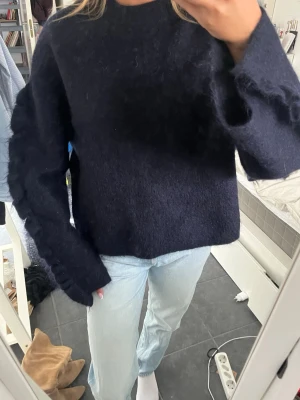 Mörkblå fluffig stickad tröja - Mörkblå stickad tröja med volang på armarna, från arket. Tröjan är helt oanvänd och i super bra kvalitet! Jätte fin med ett par shorts eller kjol nu till sommaren och perfekt på vintern till jeans💞