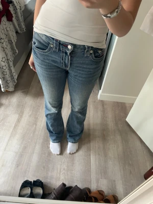 True Religion Ljusblå bootcut Jeans - Säljer ett par ljusblå bootcut jeans från True Religion, de kommer inte till användning längre. Pris går att diskutera Jeansen har snygga slitningar och röda detaljer vid fickorna. Perfekta för dig som gillar en avslappnad och trendig stil. Kan skicka fler bilder, finns några sömmar som lossnat men inget som ändrar helheten