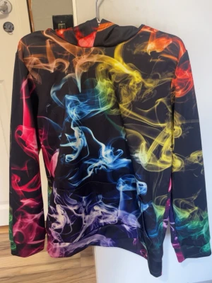 Cool hoodie - Cool svart hoodie med färgglada rök-mönster i blått, gult, rött och lila. Hoodien har huva och långa ärmar. Perfekt för dig som vill sticka ut med en unik och färgstark stil. Materialet känns mjukt och bekvämt💗Kolla in min profil för fler fina och trendiga plagg!