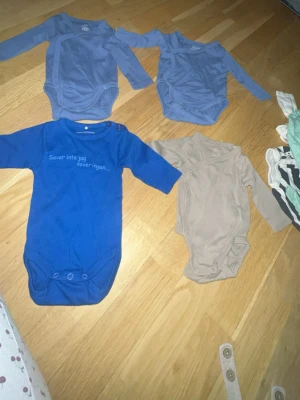 Färgglada och mönstrade babybodys - Säljer ett set med flera babybodys i olika färger och mönster. Inkluderar långärmade och kortärmade modeller i blått, beige, vitt med tryck, randigt och Disney-motiv. Perfekt för att variera stilen på de minsta. Tryckknappar i grenen för enkel påklädning.