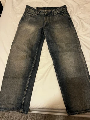 Svarta loose fit jeans med slitningar - Säljer ett par svarta loose fit jeans från H&M med snygga slitningar och tvättade detaljer. Jeansen har klassisk femficksmodell, raka ben och kontrastsömmar. Perfekta för en avslappnad och trendig stil.