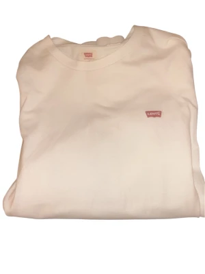 Vit hoodie från Levi's - Säljer en stilren vit sweatshirt från Levi's med klassisk rund hals och diskret röd logotyp på bröstet. Tröjan är enkel och passar perfekt till jeans eller joggers. Materialet känns mjukt och bekvämt mot huden.